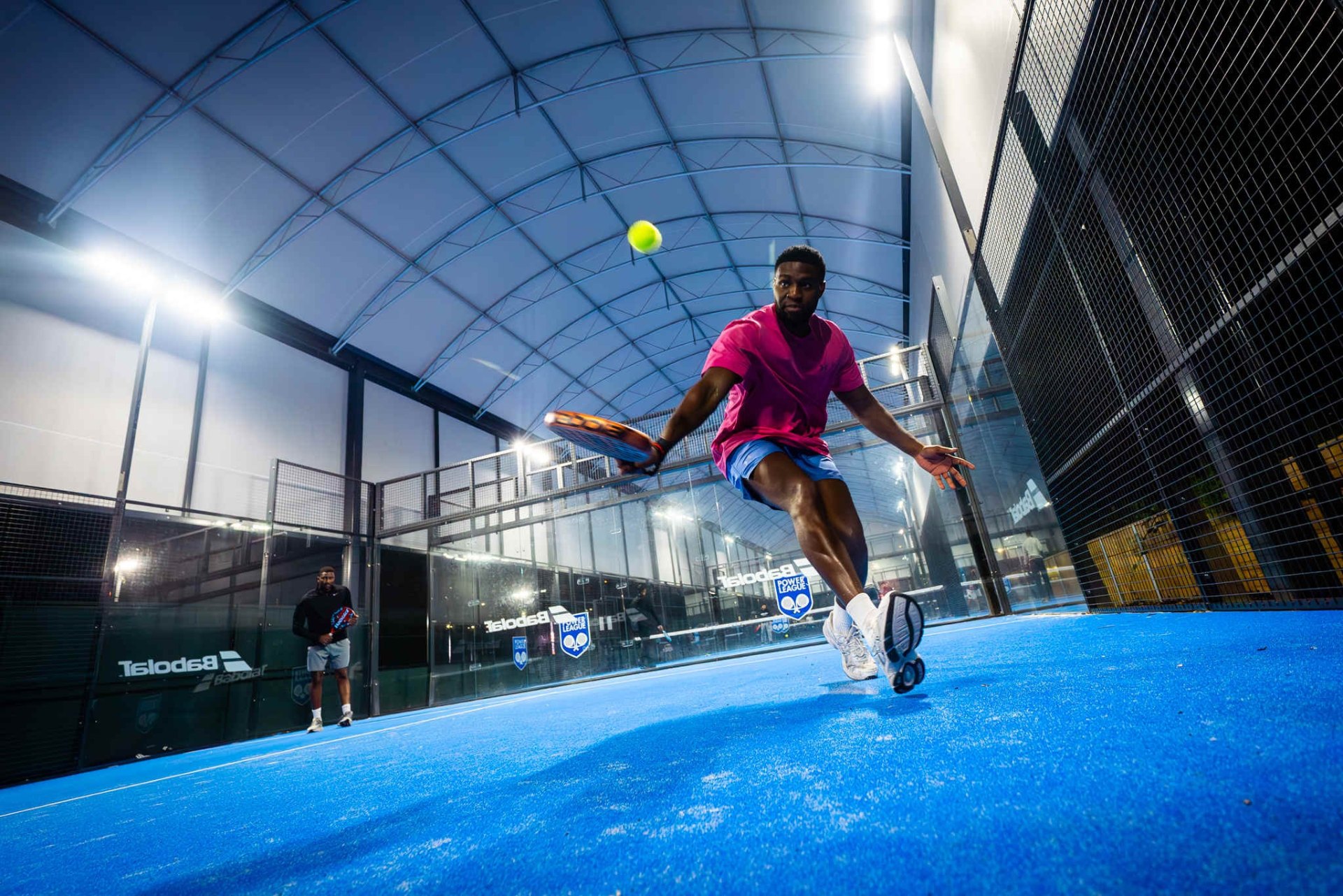 Padel player lunging for a volley on an indoor court